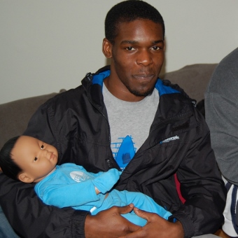 A young Afro-Caribbean man holding a 'practice' baby doll, in training for fatherhood.